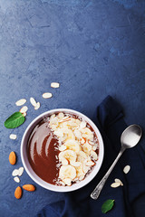 Chocolate banana almond coconut smoothie bowl on stone background top view. Healthy breakfast or dessert. Flat lay.