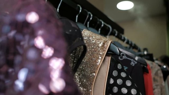 Closeup shooting clothes on rack with hangers with different colorful tissue in store. On shelf different dresses black, grey, red, blue dress, sweaters, shirts with Sequins sequins decoration rivets