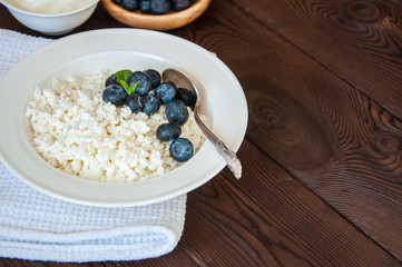 Organic Farming Cottage cheese in a white plate sour cream and blueberries on a wooden background. Copy space.