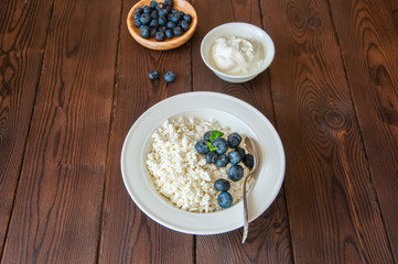 Organic Farming Cottage cheese in a white plate sour cream and blueberries on a wooden background. Copy space.