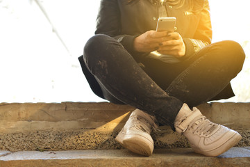 Teen girl sitting on concrete steps holding phone in hands. Teenager. Hipster. Communication. On open air. Close-up. Cropped photo
