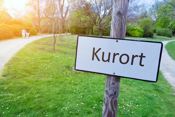 Schild `Kurort´ mit frühlingshaftem Park im Hintergrund