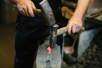 Blacksmith working metal with hammer on the anvil in the forge