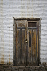 Eine alte Holztür mit Vorhängeschloss in einer weißgetünchten Steinmauer.
