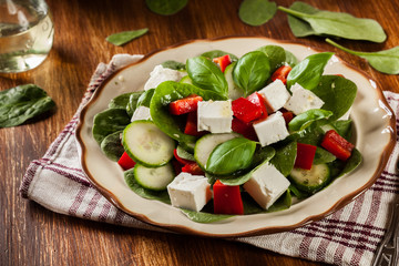 Fresh spinach salad with feta, cucumber and red paprika on a plate.