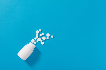 White pills spilling out of a toppled white pill bottle. Isolated on blue background. Medicine...