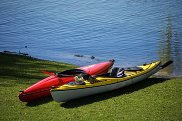 Two kayaks lie in the lawn on the shore of a lake, ready for leisure activity, copy space in the blue water