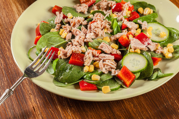 Fresh spinach salad with tuna, cucumber, corn, and red paprika on a plate