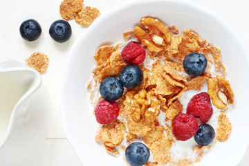 Close-up of portion of cereal with fresh berries and milk on white table. Top view.