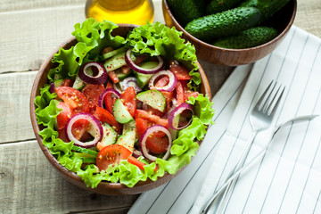 Rustic salad of fresh tomatoes, cucumbers, red onions and lettuce, dressed with olive oil and ground pepper in a wooden bowl. Top view