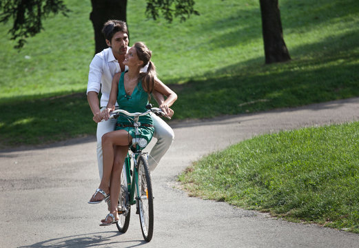 Young couple riding bicycle through park, Turin, Piedmont, Italy