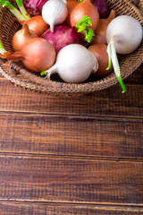 Fototapeta na wymiar Different onions in basket on wooden background. Rustic style. Copy space. Top view.
