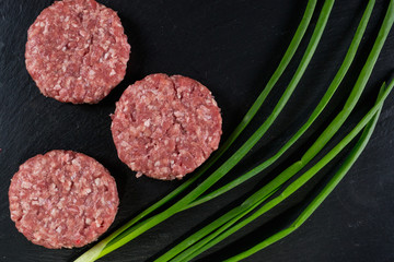 Fresh raw meat burger on the black slate board with green onion