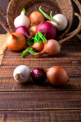 Fototapeta na wymiar Different onions in basket on wooden background. Rustic style. Red, white and golden.