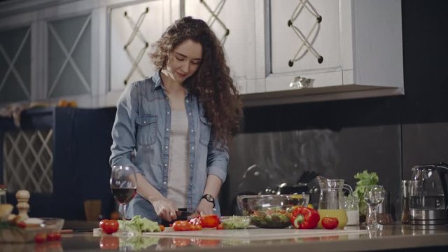 Tracking shot of young pretty woman cutting vegetables for salad on kitchen counter