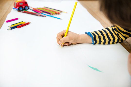 Hand of boy lying on floor drawing on long paper