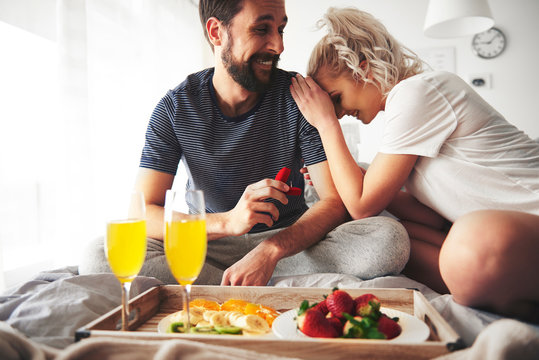 Couple sitting on bed, man proposing, holding open ring box