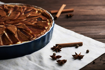 Fresh pear pie decorated with cinnamon and spices on a wooden background