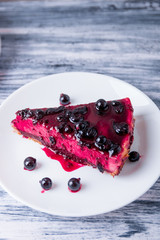 Piece of cheesecake on white plate  with currant on colored wooden background.