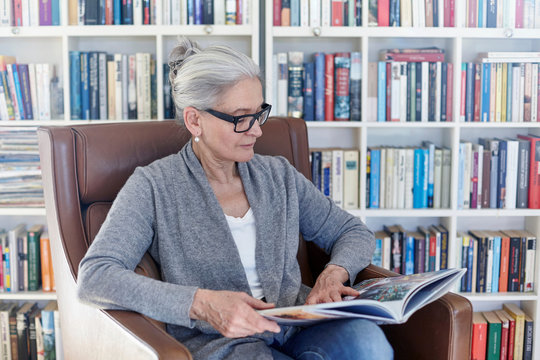 Senior woman reading book while sitting on chair in library