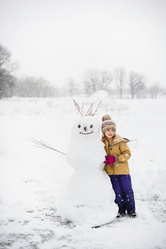 Girl shovelling snow in front of snowman, Lakefield, Ontario, Canada