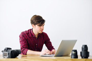 Man is working on a laptop in the office. On the table, a SLR camera and lenses