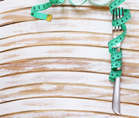 Diet concept - fork with measuring tape on a wooden table