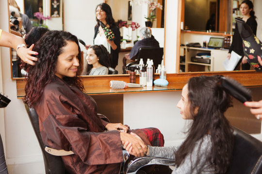 Girl and mother holding hands while having their hair styled in hair salon