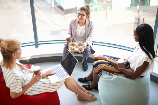 Three businesswomen with takeaway coffee sitting on beanbags chatting