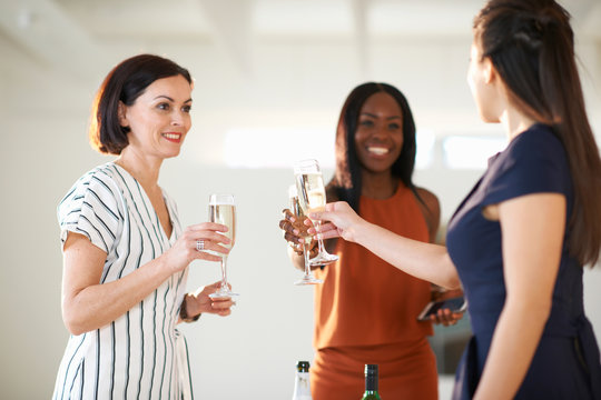 Three women raising a white wine toast at art gallery opening