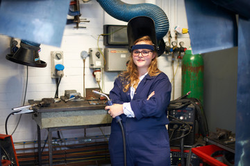 Portrait of female higher education student holding welding torch in workshop at college