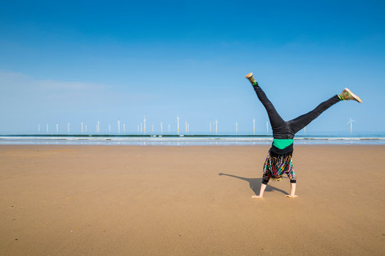 Mature woman doing cartwheel on Redcar beach, North Yorkshire, UK