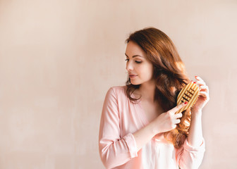 Beautiful young woman combing brushing her long smooth hair with a wooden comb. Haircare concept.