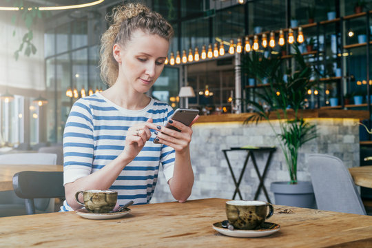 Young business woman sitting at table in cafe and using smartphone.