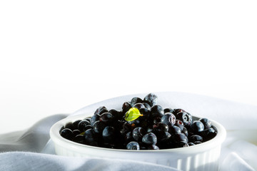 Pile blueberries in white ceramic bowl stay on white organic material.