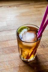 Long island iced tea cocktail with lime, ice and served with pink straw.