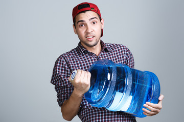 Water delivery. Cheerful young deliveryman holding a water On a gray background