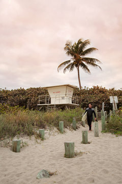 Male lifeguard walking down beach with surfboard