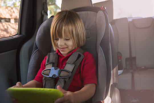 Girl in car safety seat looking at digital tablet