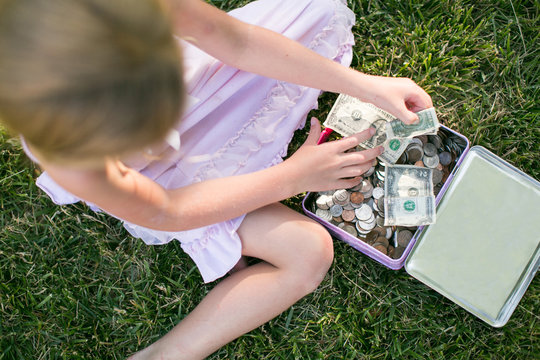 Overhead view of girl counting dollar bills on grass