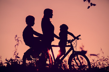 mother with son and daughter riding bike at sunset