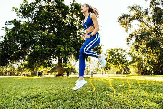 Young woman training, jumping agility hurdles in park