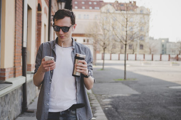 Young hipster man walking on the street and using his smartphone