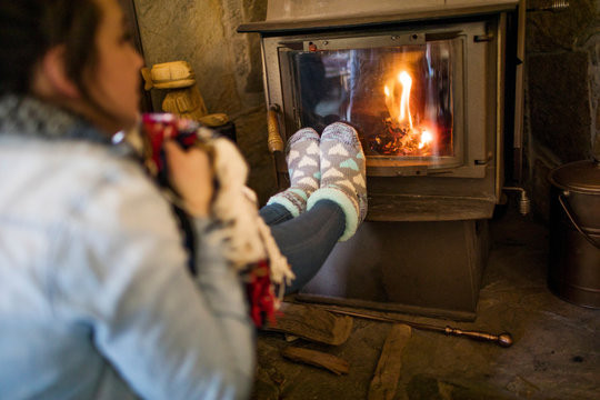 Young woman warming feet in front of fire