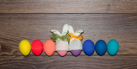 Easter eggs hand painted with knitted bunny hats over wooden background with copy space . Happy Easter