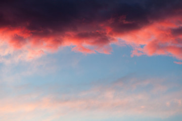 Beautiful sky background with dark blue, red stormy cloud at the top and light blue, pink sky at the bottom. Contrast pattern at sunset.