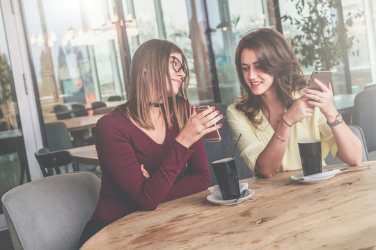 Meeting friends in a cafe. Two cheerful girls sit at a table, drink coffee and discuss news.