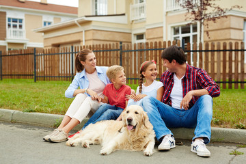 Family of new settlers talking while sitting on grass by new cottage