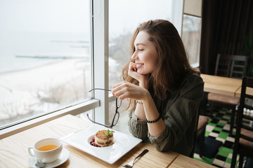 Cheerful lady with long hair holding glasses sitting in cafe.