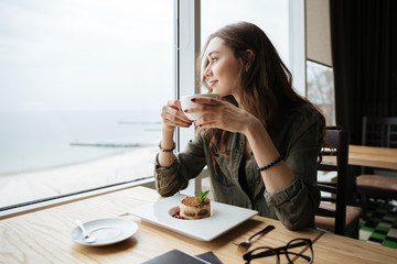 Happy young beautiful lady sitting in cafe drinking coffee.